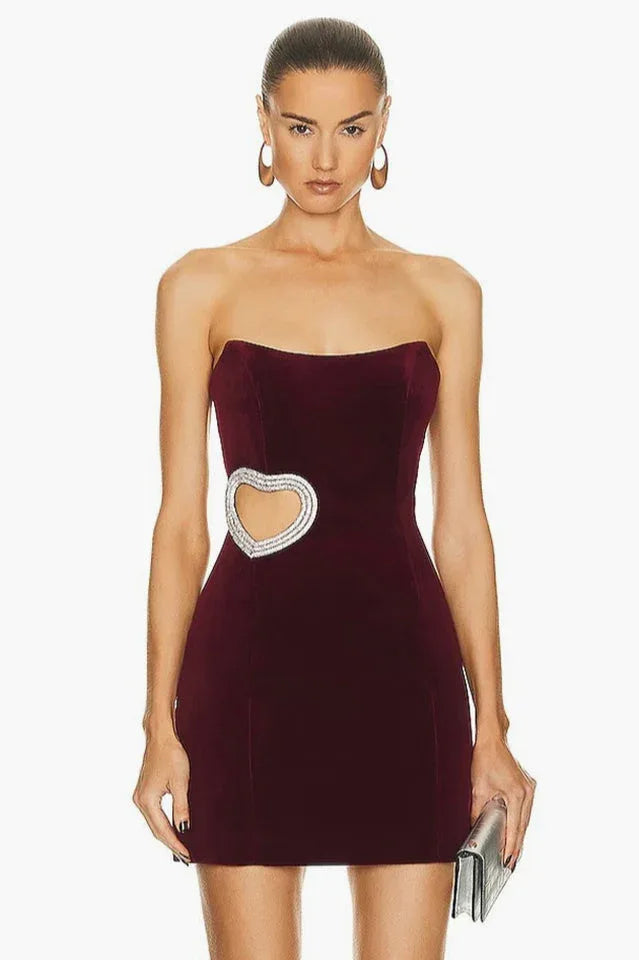 Woman wearing a burgundy velvet strapless mini dress with a heart-shaped cutout embellished with rhinestones on the side.