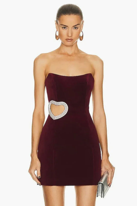Woman wearing a burgundy velvet strapless mini dress with a heart-shaped cutout embellished with rhinestones on the side.