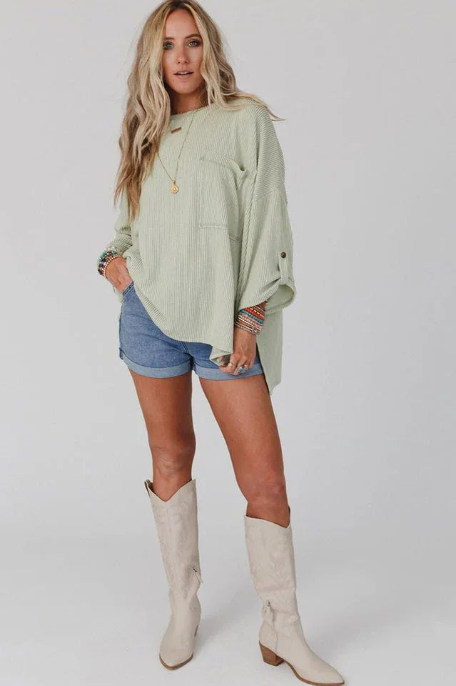 Full-length shot of a woman in a light green ribbed top, denim shorts, and cream boots.