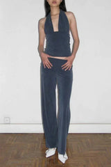 Full body shot of a woman wearing a dark blue halter neck crop top and dark blue wide leg pants, with white pointed-toe shoes.