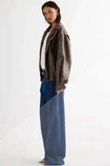 Side view of a model in a brown faux leather jacket, white tank top, and blue wide-leg jeans