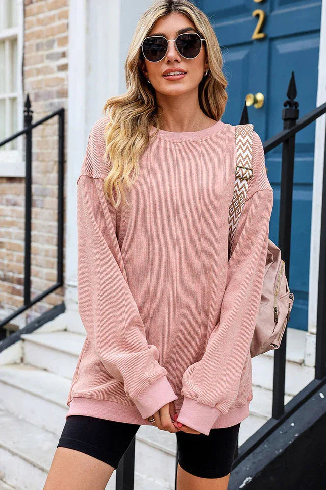 Woman wearing a pink ribbed long-sleeve oversized tunic and black shorts, with a patterned strap bag