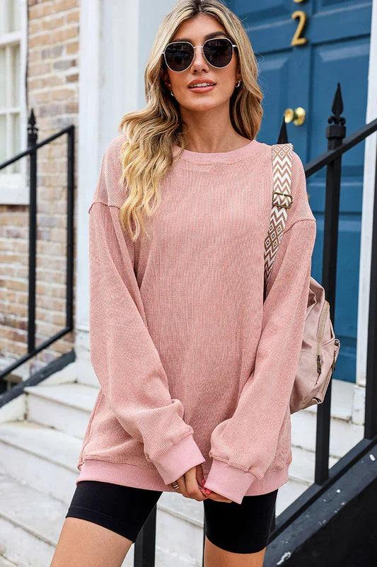 Woman wearing a pink ribbed long-sleeve oversized tunic and black shorts, with a patterned strap bag
