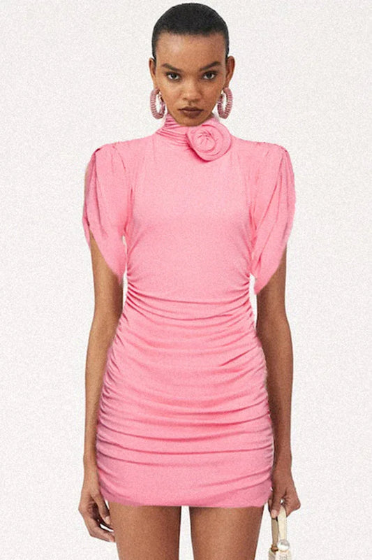 Model wearing a pink ruched mini dress with a mock neck and floral applique