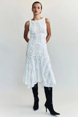 Front view of a woman wearing a white crochet knit cropped tank top and a white crochet knit asymmetrical hem midi skirt with black boots.