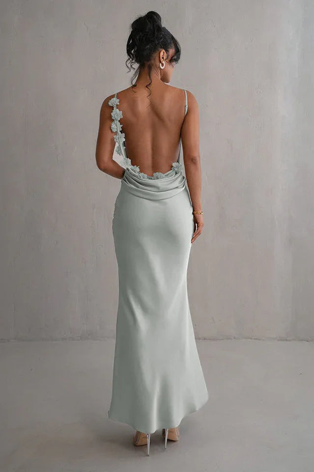 back view of a woman wearing a light green satin floor-length mermaid dress with a low back and floral embellishments on the straps