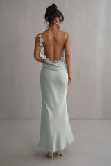 back view of a woman wearing a light green satin floor-length mermaid dress with a low back and floral embellishments on the straps