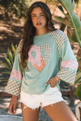 Woman wearing a mint green long-sleeved top with a heart applique and plaid patchwork sleeves, paired with white denim shorts.