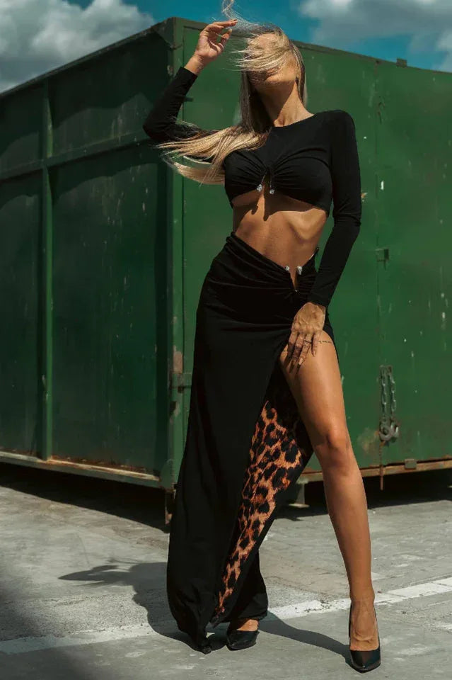 Woman wearing a black long-sleeve crop top and a black maxi skirt with a high slit and leopard print lining.