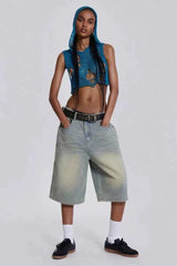 Woman with hands in pockets wearing a blue distressed knit crop top with a hood and light wash wide-leg denim capri pants, a black belt, white socks, and black sneakers.