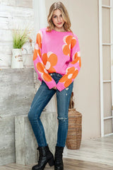Full body shot of a woman wearing a pink crew neck sweater with an orange and white floral print, blue jeans, and black boots.