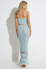 Rear view of a woman wearing a light blue knit maxi dress with a halter neckline and cut-out detail.