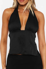Woman wearing a black satin halter top with a deep V-neck and black skirt.