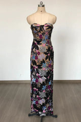 A strapless, floor-length column dress with a sweetheart neckline displayed on a mannequin. The dress is embellished with colorful floral appliques and sequins.