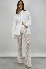 Full-body shot of a woman in a white oversized button-down shirt and white lace wide-leg pants, standing.