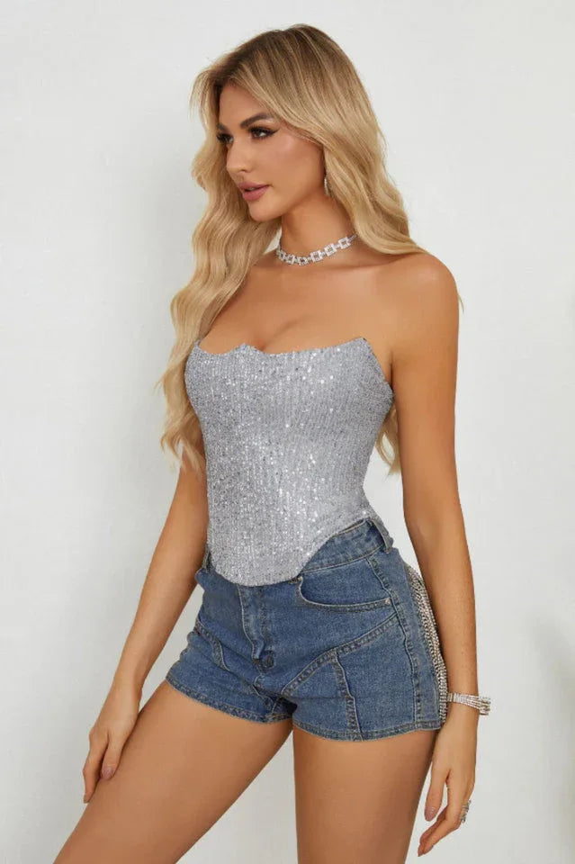 Rear view of a woman wearing a silver sequined strapless corset top and blue denim shorts with fringe detailing.