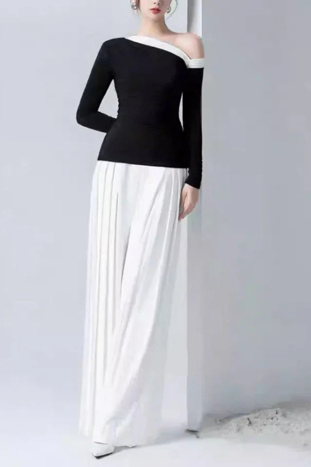 Back view of a model in a black asymmetrical top and white wide-leg pleated pants.