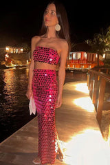 Woman wearing a pink sequined strapless top and matching full-length skirt on a wooden pier at night.