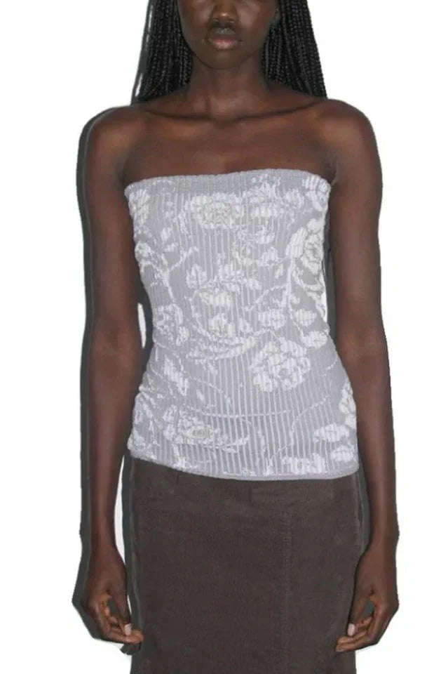 Woman wearing a light gray strapless top with a white floral pattern and vertical ribbing, paired with brown pants.