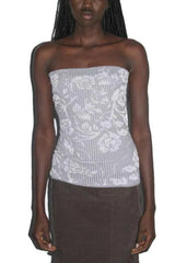 Woman wearing a light gray strapless top with a white floral pattern and vertical ribbing, paired with brown pants.