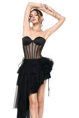 Woman posing in a black strapless corset dress with an asymmetrical ruffled skirt and tulle train.