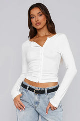 Woman wearing a white long-sleeve cropped top with button-up front and blue jeans