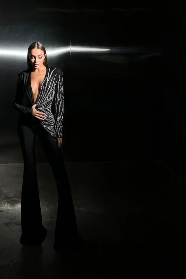 Model standing in a dimly lit setting, wearing a black jumpsuit with a striking sequin design.