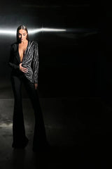 Model standing in a dimly lit setting, wearing a black jumpsuit with a striking sequin design.