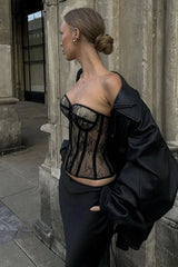Woman wearing a black lace corset top and a black skirt, with a black jacket draped over her shoulders
