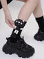 A person is holding a black sock with a cat applique on it, with black platform shoes in the foreground.