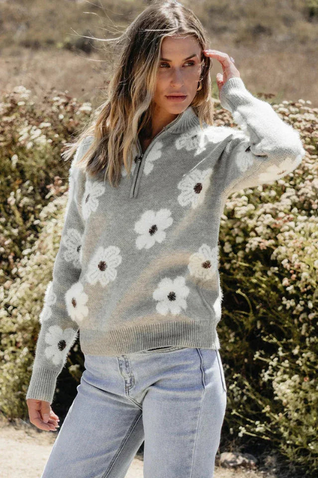 Woman in profile wearing a gray floral print quarter-zip knit sweater and light wash denim jeans.