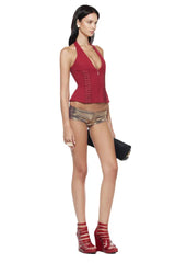 Side view of a model wearing a red halter corset top with gold shorts and red strappy heels.