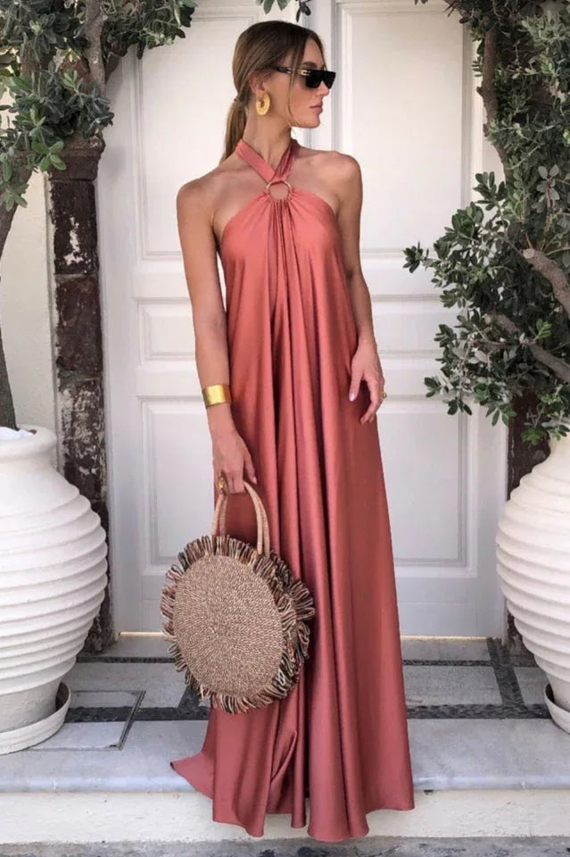 Woman wearing a coral satin halter maxi dress and carrying a straw bag.