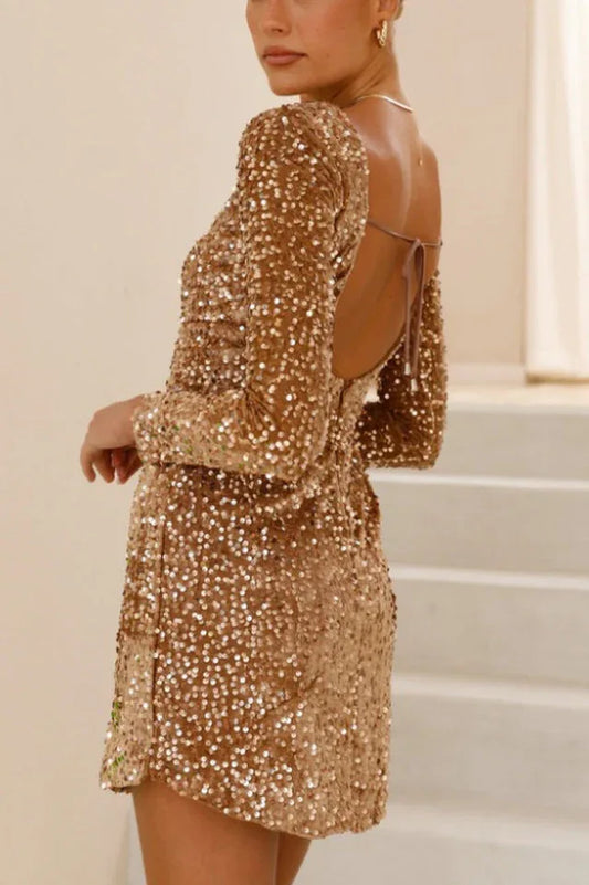 Woman wearing a gold sequin mini dress with long sleeves and an open back