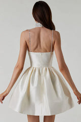Back view of a woman in a short, ivory satin dress with a sweetheart neckline, embellished spaghetti straps, and a full A-line skirt.