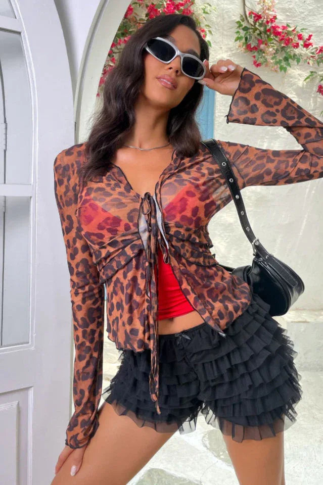 Woman wearing a leopard print sheer mesh top with a red bralette and black ruffled shorts.