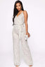 Woman wearing a silver sequined sleeveless wrap jumpsuit with a self-tie waist belt and wide legs, holding a silver clutch.