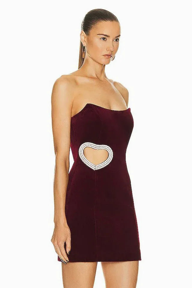 Side view of a woman in a burgundy velvet strapless mini dress featuring a heart-shaped cutout with embellishments.
