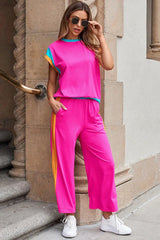 Woman wearing a bright pink two-piece set with blue and orange accents, standing outdoors, adjusting sunglasses.