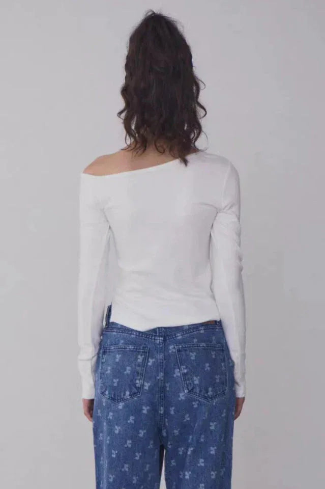 Woman wearing a white off-the-shoulder long-sleeve top with a black beanie and blue patterned jeans, back view.