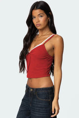 Side view of a red cropped tank top with lace trim and a tie front, paired with dark wash jeans.