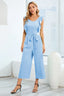 Woman wearing a light blue wide leg culotte jumpsuit with ruffle sleeves and a self-tie waist, paired with black strappy heels.