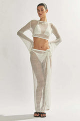 Model wearing a white sheer knit cropped long-sleeve top, bikini, and a matching white sheer knit maxi skirt with a high slit.
