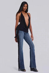 Full body shot of a model wearing a black halter top with a deep V-neck and studded trim, paired with blue flared jeans with fringe detailing.