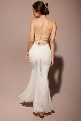Back view of a woman wearing a white lace mermaid wedding dress with spaghetti straps and a low back with criss-cross ties, walking away.