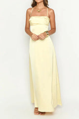 woman wearing a pale yellow satin maxi dress with spaghetti straps and a sweetheart neckline, hands clasped in front