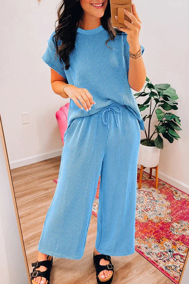Woman taking a mirror selfie in a blue ribbed short-sleeve top and wide-leg pants.