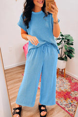 Woman taking a mirror selfie in a blue ribbed short-sleeve top and wide-leg pants.