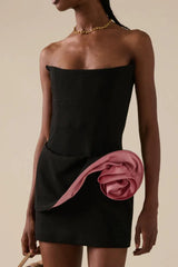 Close-up of a black strapless mini dress with a pink rose embellishment on the side.