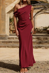 Full length portrait of a woman in a burgundy one-shoulder satin maxi dress.